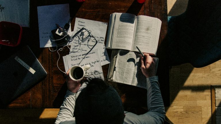 Muškarac rukom zapisuje bilješke na list papira za stolom