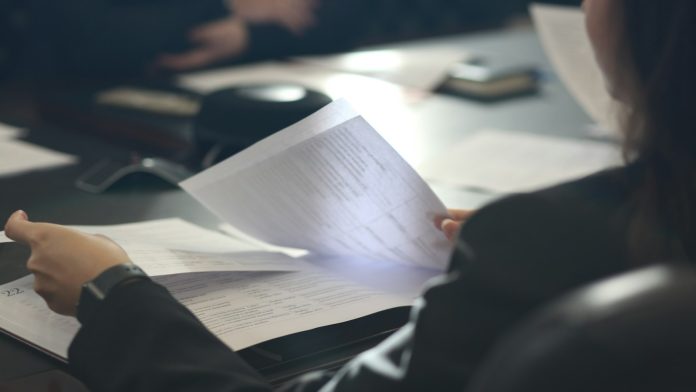Osoba za stolom čita ispisani dokument