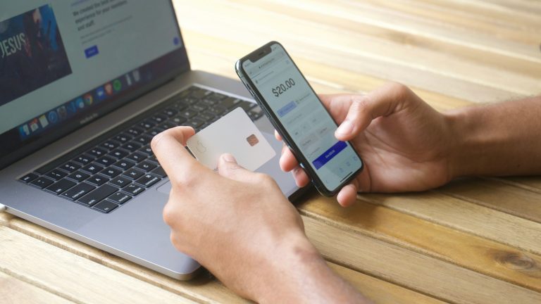 Ruke drže pametni telefon i platnu karticu ispred prijenosnog računala