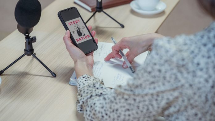 Osoba koristi mobitel za stolom s mikrofonima i bilješkama