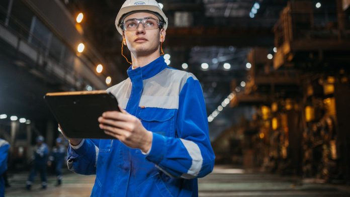 Inženjer sa zaštitnom opremom pregledava tablet u industrijskom prostoru