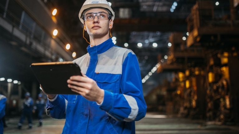 Inženjer sa zaštitnom opremom pregledava tablet u industrijskom prostoru