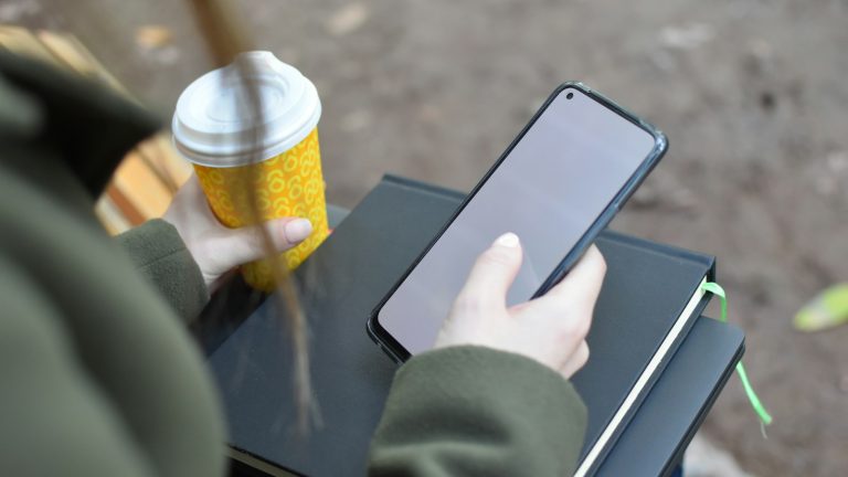 Ruke drže pametni telefon pokraj šalice kave