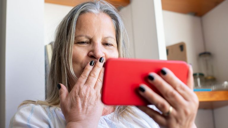 Starija žena drži pametni telefon i razgovara u kućnom prostoru
